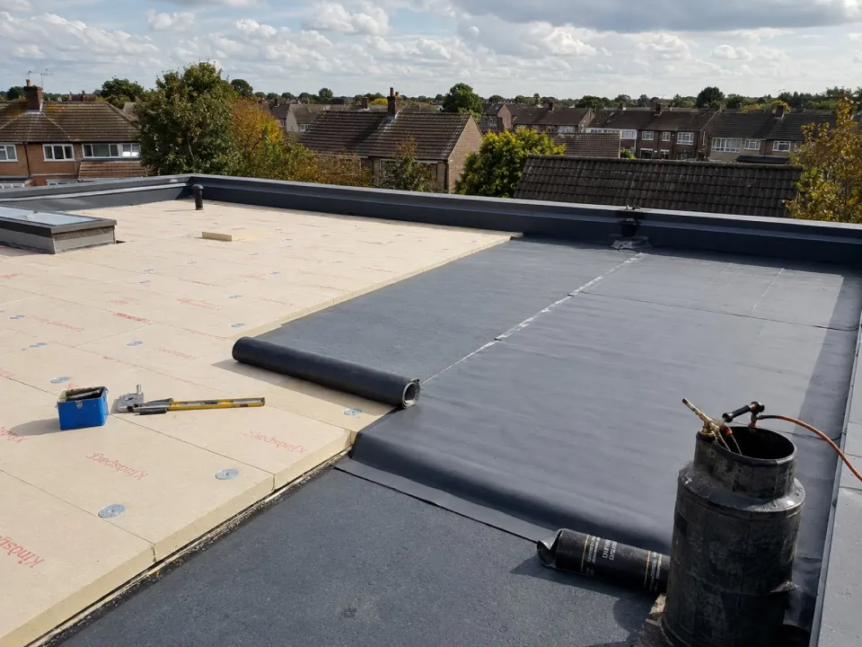 New flat roof insulation boards and membrane being installed, with a torch and primer ready for the seams